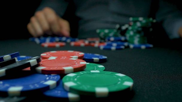 Ρίχνουν των μπλε μάρκες πόκερ. Μπλε και κόκκινο παίζοντας πόκερ μάρκες στο αντανακλαστικό μαύρο φόντο. Κοντινό πλάνο του πόκερ μάρκες σε στοίβες στην Πράσινη τσόχα κάρτα πίνακα επιφάνεια σε αργή κίνηση - Φωτογραφία, εικόνα