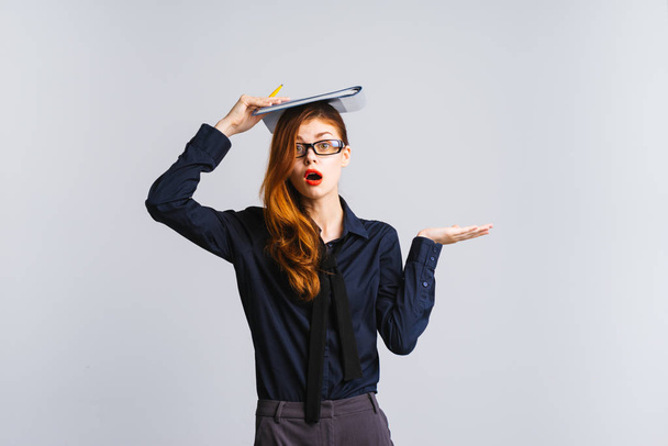 surprised red-haired lady with glasses holding a folder on her head, isolated - Foto, afbeelding