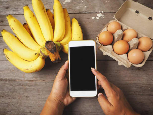Femme utilisant un téléphone intelligent avec des œufs et des bananes
 - Photo, image