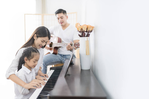 Aasialainen perhe, äiti ja tytär pelaa pianoa, isä pelaa
  - Valokuva, kuva