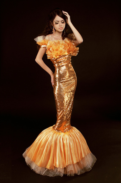 Young brunette lady in golden gorgeous dress posing on black bac - Foto, afbeelding