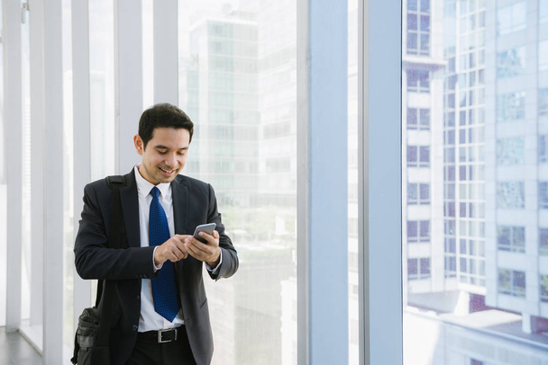 Man on smart phone - young businessman in airport. Casual urban professional business man using smartphone smiling happy inside office building. Handsome man wearing suit jacket indoors. - Zdjęcie, obraz