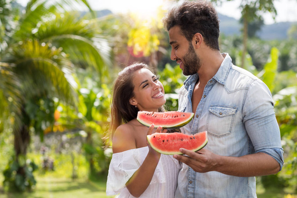 Happy Couple Embracing Looking At Each Other Hold Watermelon Slice Outdoors In Tropical Park Attractive Man and Woman - Foto, immagini