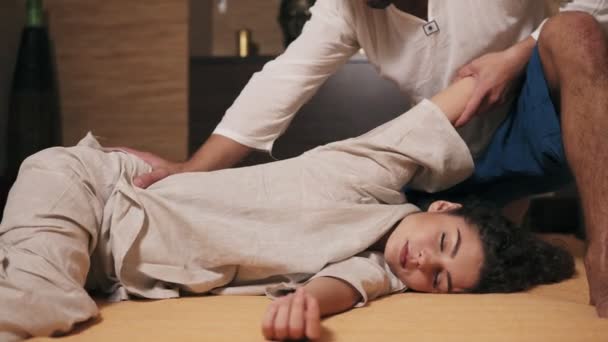 Young attractive woman with her eyes closed is receiving thai massage. Male thai massagist is stretching womans hand and side. Shot in 4k - Πλάνα, βίντεο