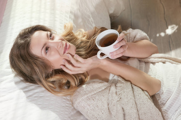 Woman lying on bed with cup of tea - Fotoğraf, Görsel