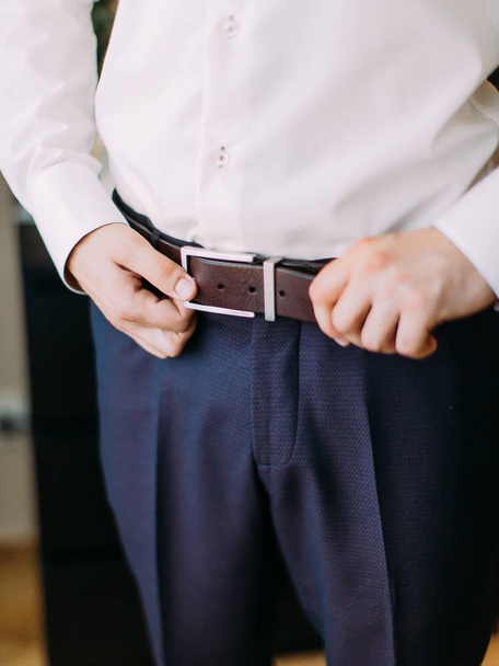 The hands of the groom are correcting the leather belt. - Foto, Imagen