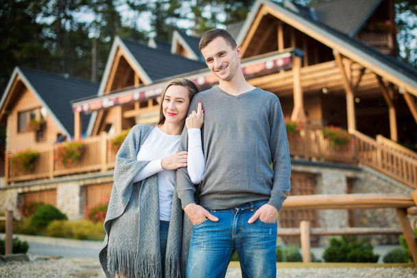 Young attractive married couple standing outside their large wooden cottage in the woods. - Foto, Imagem