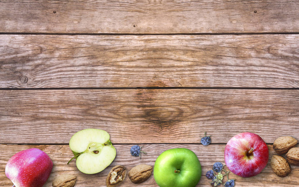 Ημέρα των Ευχαριστιών με μήλα, καρύδια και μούρα σε ένα παλιό ξύλινο φόντο. Ημέρα των Ευχαριστιών με εποχιακά μούρα και φρούτα. Έννοια της εξαιρετικής περιόδου εσοδείας. Φθινοπωρινό φόντο. - Φωτογραφία, εικόνα