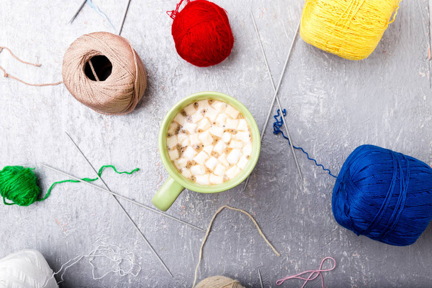 Multicolor knitting ball and needles around green cup of coffee  on grey background. Top view. Copy space. Knitting yarn. - Photo, Image