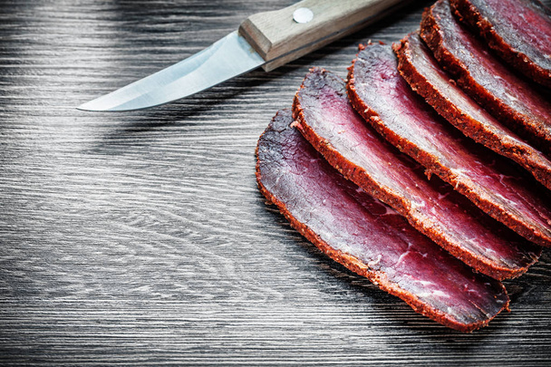 Cuchillo de carne ahumada en rodajas sobre tabla de madera
 - Foto, Imagen