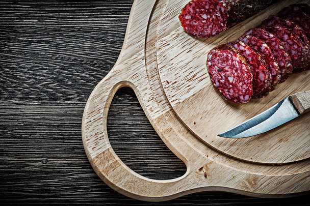 Sliced salami knife on wooden carving board - Фото, изображение