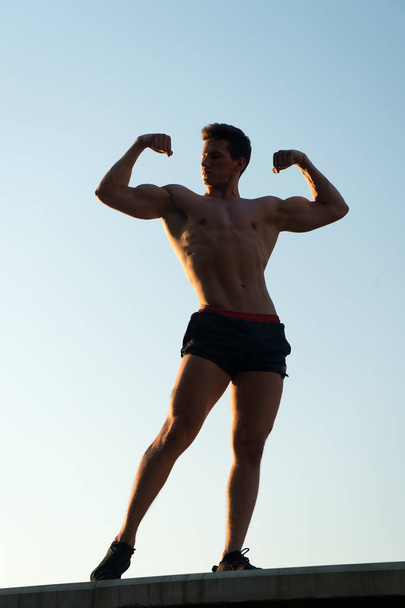 Man showing fit body on blue sky - Фото, изображение