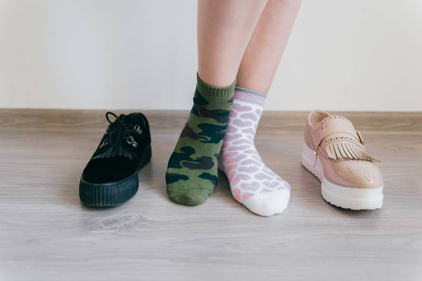 Female naked legs standing on floor. Women`s feet in missmatched cotton socks. Odd unusual weird unrecognizable bizarre kinky girl. Brutal and tenderness concept. Different big choice of footwear.  - 写真・画像