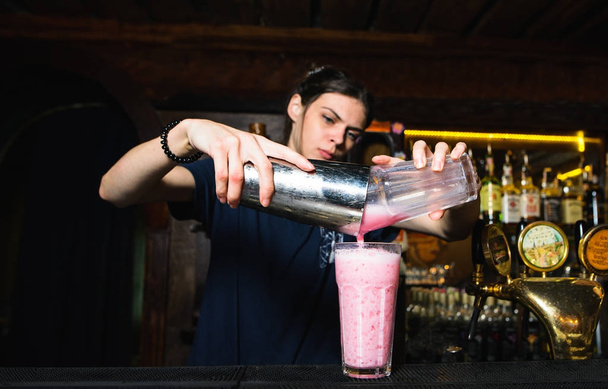 Девушка-бармен создает красивый, розовый, алкогольный коктейль. Бармен наливает ингредиенты из шейкера в стакан
 - Фото, изображение