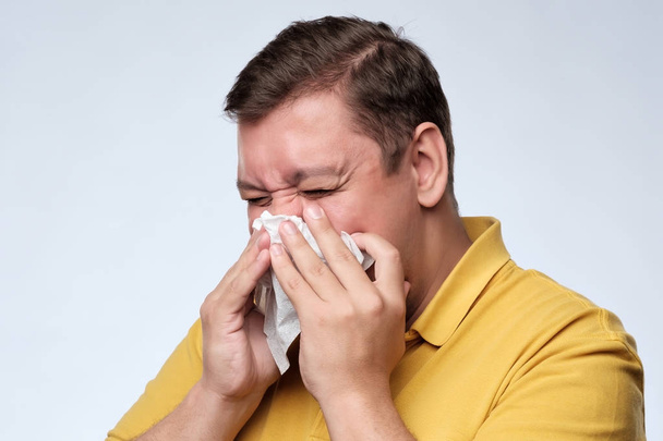 Mature fat caucasian man is ill from colds or pneumonia, sneezing in napkin. - Photo, Image