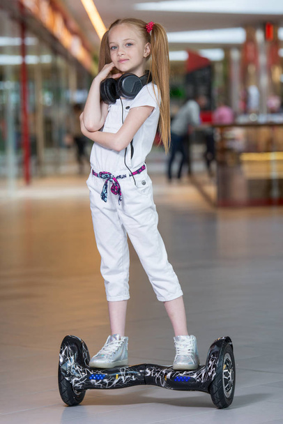 Happy and smiling girl rides on mini segway in the headphones at trading mall. Teenager riding on hover board or gyroscooter and listening to music. - Foto, immagini