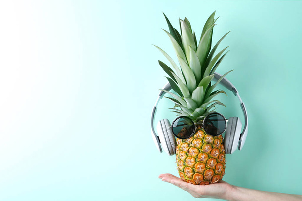 Female hand holding pineapple with sunglasses and headphones  - 写真・画像