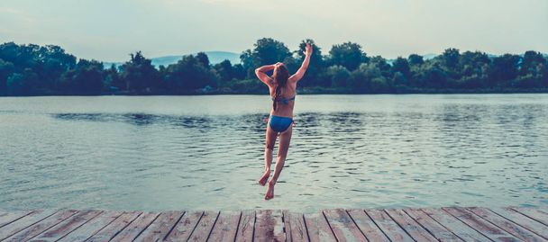 Girl jumping into water from dock - Foto, afbeelding