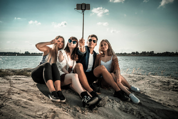 Группа друзей, делающих автопортрет с селфи-палкой, развлекающихся на пляже
 - Фото, изображение