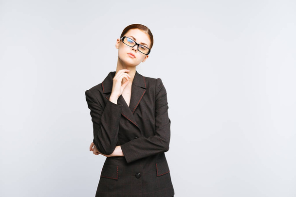A strict lady in a suit and wearing glasses looks at the camera on a white background - Fotó, kép