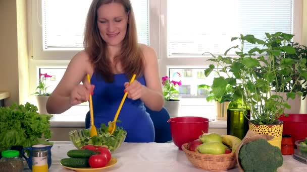 madre embarazada sonriente usando dos cucharas para preparar y mezclar ensalada de verduras
 - Metraje, vídeo