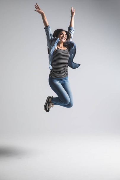 Hravá mladá žena nosí, neformální skoky přes šedé pozadí. Podívejte se na kameru a křičí. - Fotografie, Obrázek
