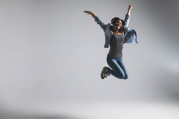 Mujer joven juguetona que usa saltos casuales sobre fondo gris. Mira la cámara y grita
. - Foto, imagen