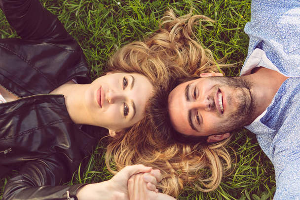 Вид сверху на двух друзей, улыбающихся, глядя в небо, когда они лежат на траве
. - Фото, изображение