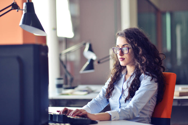 Portrait of smiling pretty young business woman in glasses sitting on workplace - Φωτογραφία, εικόνα