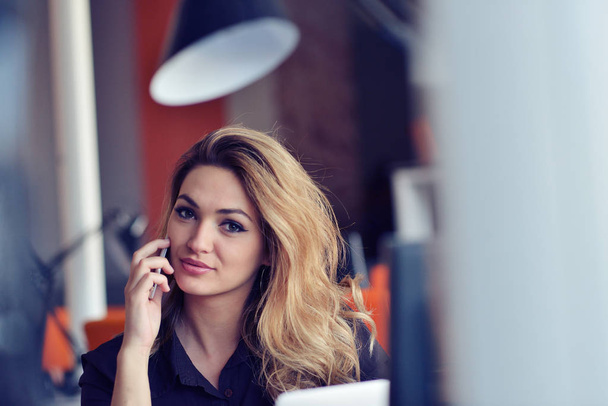 Happy beautiful young business woman sitting and talking on cell phone in office - Fotó, kép
