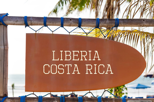 Pomarańczowy szyld vintage w kształt deski surfingowej z Liberii, Costa Rica tekst dla surf spot i palmy w tle - Zdjęcie, obraz