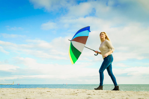 Woman holding colorful umbrella on beach - 写真・画像