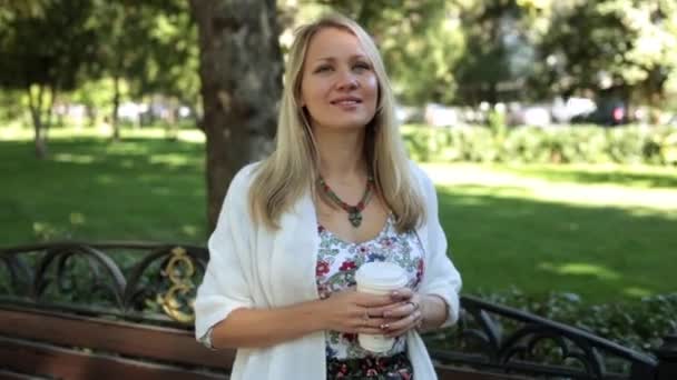 Beautiful young woman is walking outdoors and drinking coffee or tea. - Video