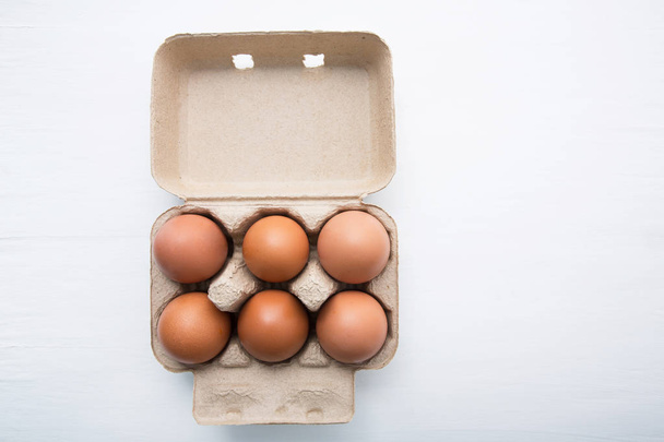 Chicken eggs in egg box on white wooden background. - Photo, Image
