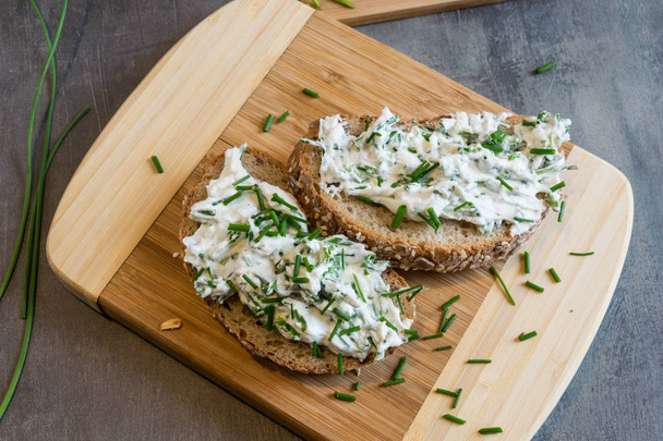 Home made bread on a wooden cutting board with curd cheese and ricotta and herbs. Decorated with green herbs  - Photo, Image