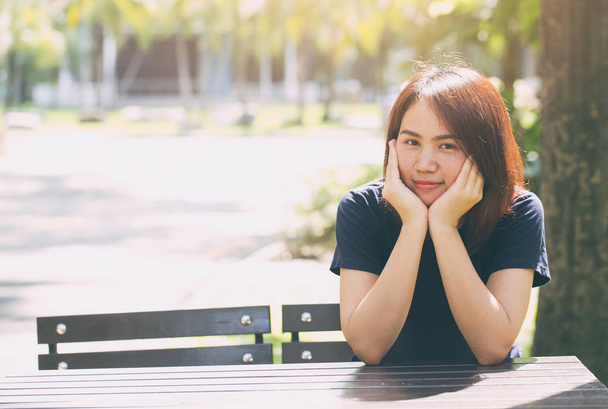 Asiatico giovanissima casual panno seduta sorriso con mano hold su faccia in il verde parco sano concetto
 - Foto, immagini