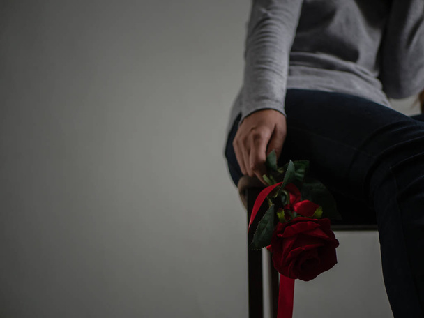 Λυπημένη γυναίκα κάθεται και κλαίει με κόκκινο τριαντάφυλλο στο χέρι. - Φωτογραφία, εικόνα