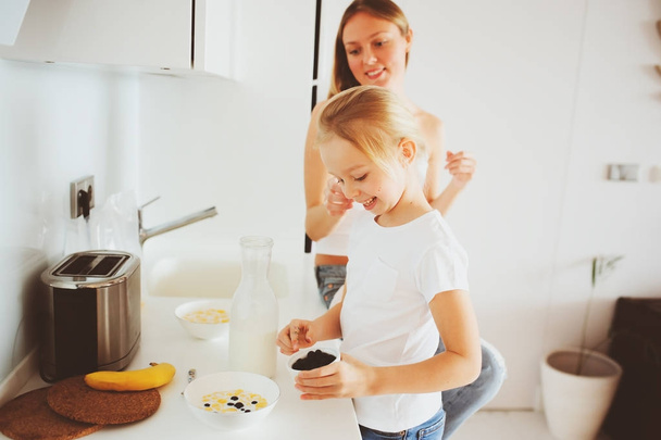 mother having breakfast with kid daughter at home in modern white kitchen, cozy lifestyle in the morning - Foto, afbeelding