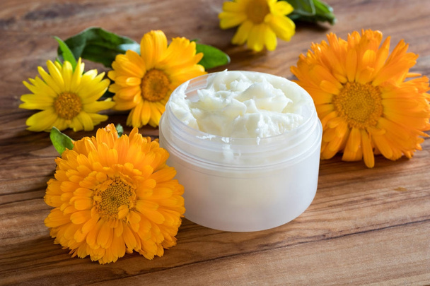 A jar of calendula cream, with calendula flowers in the backgrou - Photo, Image