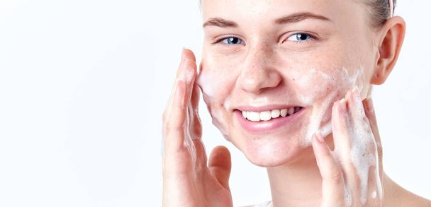 Teenager skincare. Smiling beautiful teen girl with freckles and blue eyes using foaming cleanser. Face washing concept isolated on white background. - Photo, Image