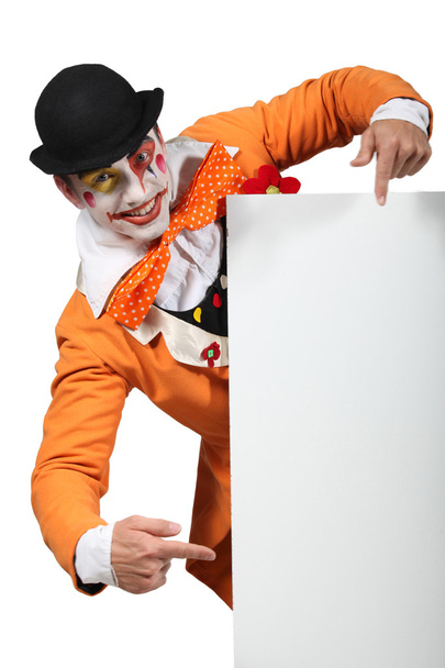 Homem vestido como um brincalhão apontando para uma placa deixou em branco para sua imagem
 - Foto, Imagem