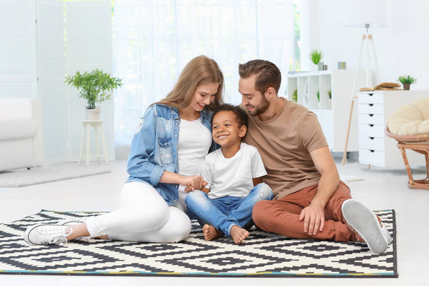Happy couple with adopted African-American boy sitting on carpet at home - Foto, Imagen