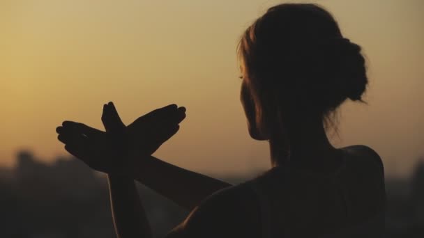 Silhouette einer Frau machen Adlervogel aus Händen, die im hohen Stock Balkon bei Sonnenuntergang stehen - Filmmaterial, Video