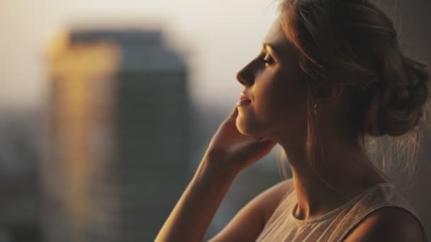 Pensando giovane donna che guarda al paesaggio della città e edificio in piedi nel balcone al piano superiore al tramonto
 - Filmati, video