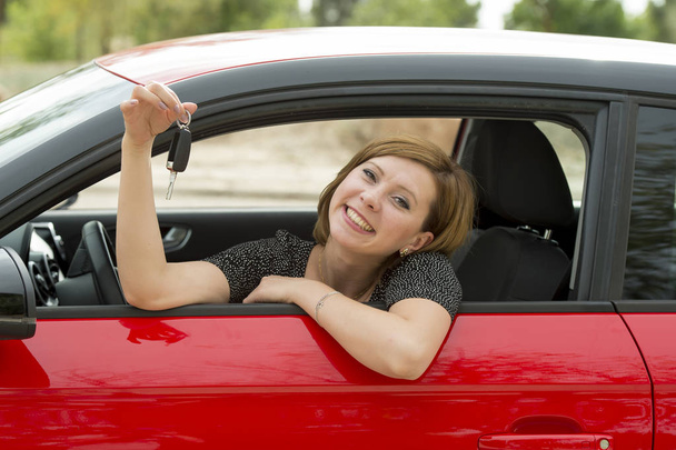 ελκυστική γυναίκα χαμογελώντας περήφανοι κάθεται στο κάθισμα οδηγού κρατώντας και δείχνοντας το κλειδί του αυτοκινήτου στο νέο αυτοκίνητο για αγορά και ενοικίαση - Φωτογραφία, εικόνα