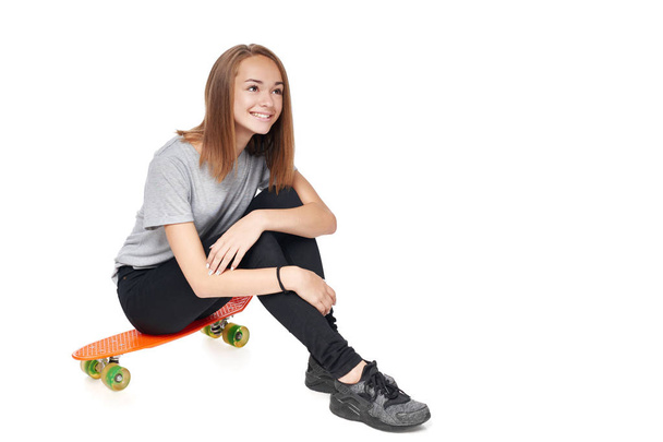 Teen girl in full length sitting on skate board - Фото, изображение