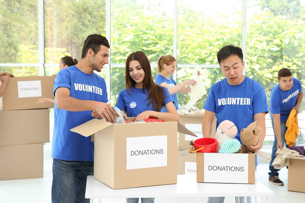 Team of teen volunteers collecting donations in cardboard boxes indoors - Photo, Image