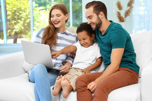 Happy couple with adopted African-American boy using laptop while sitting on couch at home - Foto, immagini