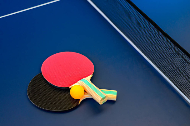 Настільний тенісний стіл з ракетками та помаранчевим м'ячем
  - Фото, зображення