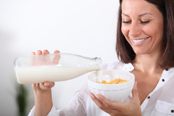 Woman pouring milk onto a bowl of cereal - Zdjęcie, obraz